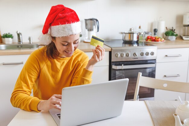 Kobieta w Santa hat zakupy online i płacenie złotą kartą kredytową