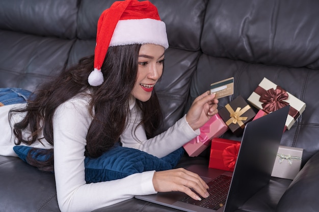 Kobieta w Santa kapeluszu robi zakupy online dla Bożenarodzeniowego prezenta z laptopem w żywym pokoju