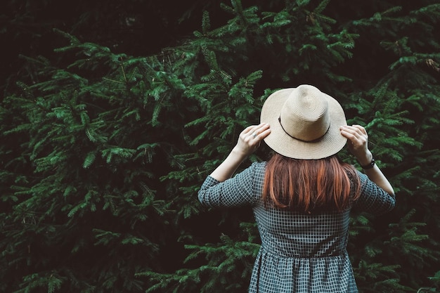 Kobieta w słomkowym kapeluszu i sukience na tle zielonych drzew