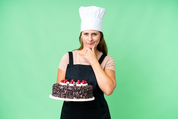 Kobieta w średnim wieku, cukiernik, trzymająca duży tort na odosobnionym tle myślenia