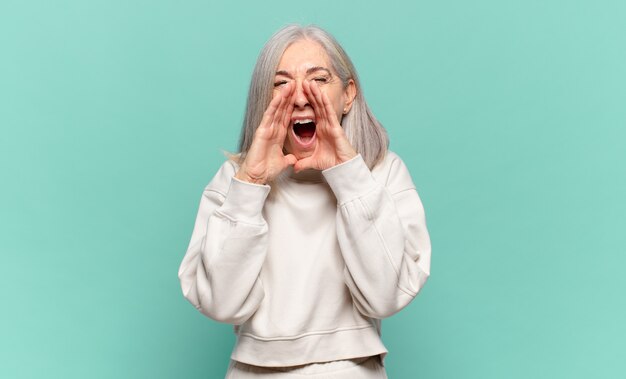Kobieta w średnim wieku czująca się szczęśliwa, podekscytowana i pozytywna, krzycząca głośno z rękami przy ustach