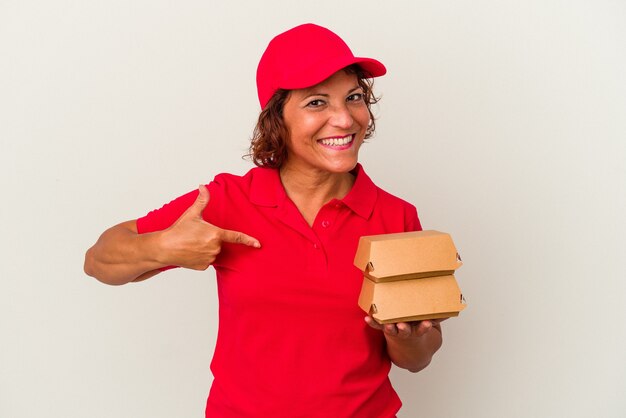 Kobieta w średnim wieku dostarczająca hamburgery na białym tle osoba wskazująca ręcznie na miejsce na koszulkę, dumna i pewna siebie