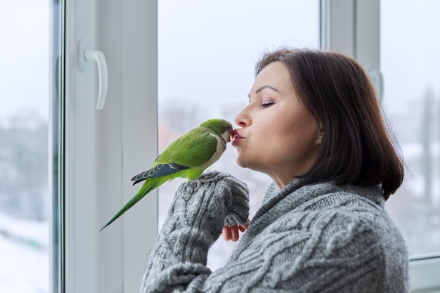 Kobieta w średnim wieku i papuga razem właścicielka ptaka rozmawiająca całująca zielone zwierzę mnichów