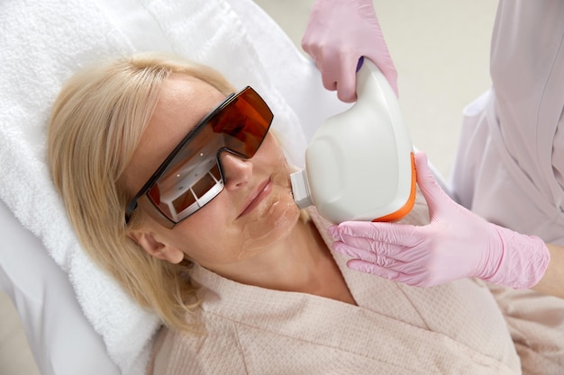 Kobieta w średnim wieku otrzymująca leczenie laserowe w klinice kosmetologicznej w okularach ochronnych