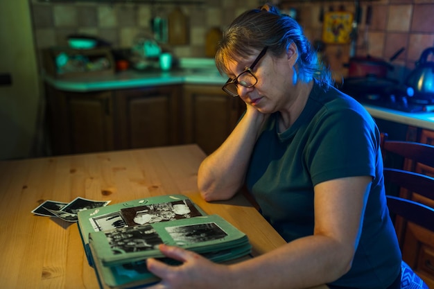 Kobieta w średnim wieku patrząca na rodzinny album ze zdjęciami Nostalgia smutek wspomnienia w średnim wieku koncepcja