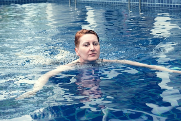 Kobieta w średnim wieku pływa w basenie i uśmiecha się