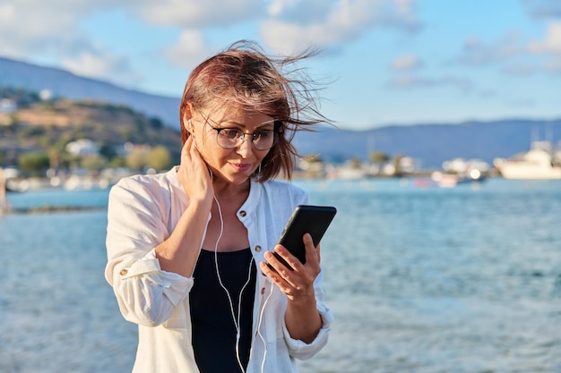 Kobieta w średnim wieku relaksująca się na plaży w słuchawkach ze smartfonem