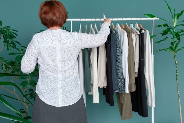 Kobieta w średnim wieku robi zakupy i patrzy na nową sukienkę przy półce z ubraniami.