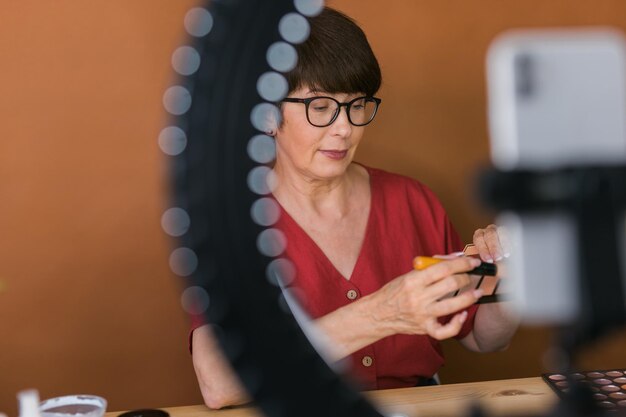 Kobieta w średnim wieku rozmawia o kosmetykach z cieniami do makijażu i paletą różu i pędzlami, podczas gdy re