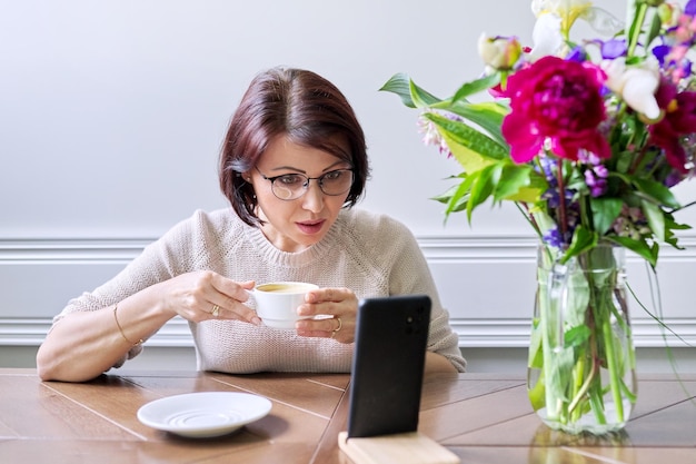 Kobieta w średnim wieku siedzi w domu i używa smartfona do relaksu