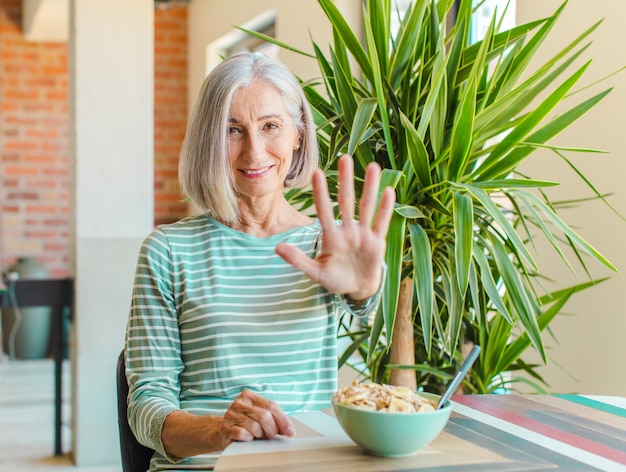 Kobieta w średnim wieku, uśmiechnięta i przyjazna, pokazująca cyfrę pięć lub piąty z ręką do przodu, odliczająca
