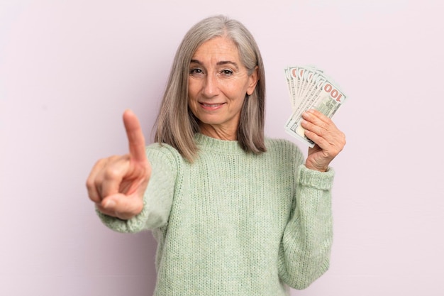 Kobieta w średnim wieku uśmiechnięta i wyglądająca przyjaźnie, pokazująca koncepcję banknotów dolarowych numer jeden