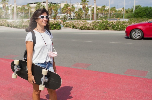 Kobieta w średnim wieku w okularach przeciwsłonecznych, ciesząca się jazdą na deskorolce na ulicy.