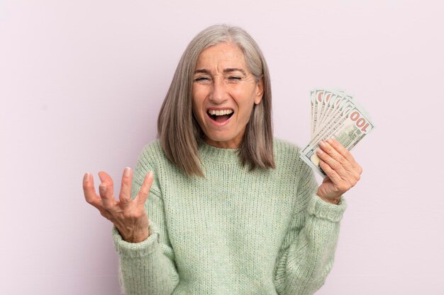 Kobieta w średnim wieku wygląda na złą, zirytowaną i sfrustrowaną koncepcję banknotów dolarowych