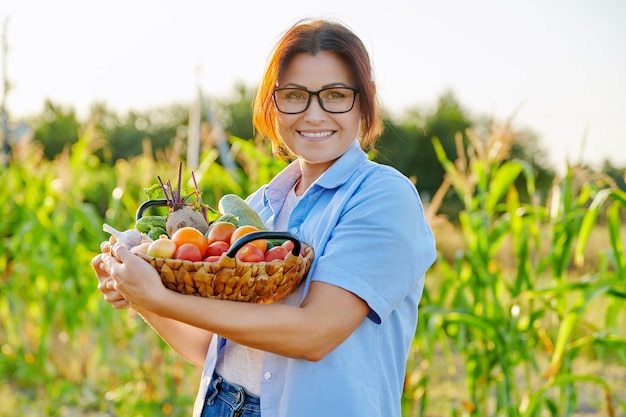 Kobieta w średnim wieku z koszem świeżych organicznych warzyw w gospodarstwie ogrodowym