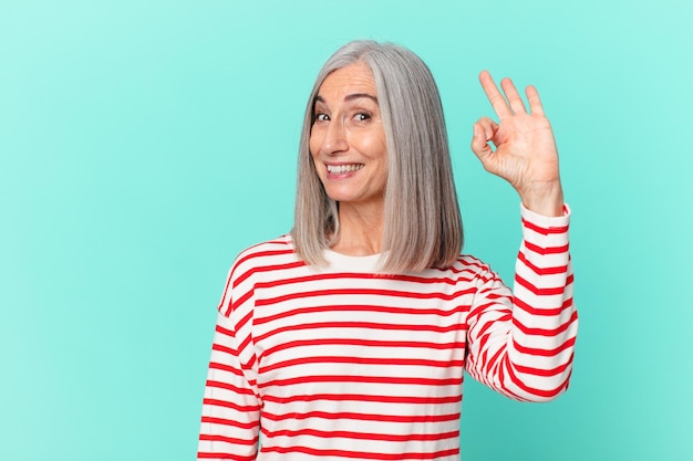 Kobieta w średnim wieku z siwymi włosami czuje się szczęśliwa, okazując aprobatę dobrym gestem