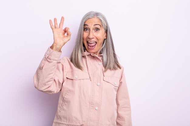 Zdjęcie kobieta w średnim wieku z siwymi włosami, która czuje się dobrze i jest zadowolona, uśmiecha się z szeroko otwartymi ustami, robiąc dobry znak ręką