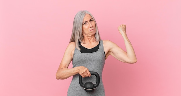 Kobieta w średnim wieku z siwymi włosami podnosząca koncepcję fitness z hantlami