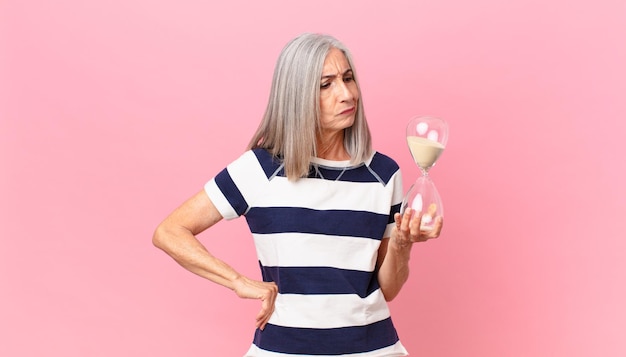 Zdjęcie kobieta w średnim wieku z siwymi włosami trzymająca zegar z klepsydrą