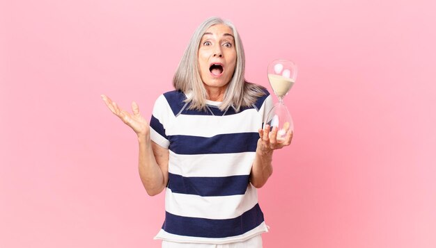 Kobieta w średnim wieku z siwymi włosami trzymająca zegar z klepsydrą