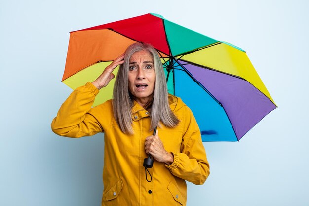 kobieta w średnim wieku z siwymi włosami, wyglądająca na szczęśliwą, zdumioną i zdziwioną. koncepcja parasola i deszczu