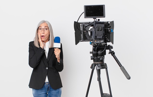 Kobieta w średnim wieku z siwymi włosami, zszokowana i przestraszona, trzyma mikrofon. koncepcja prezentera telewizyjnego