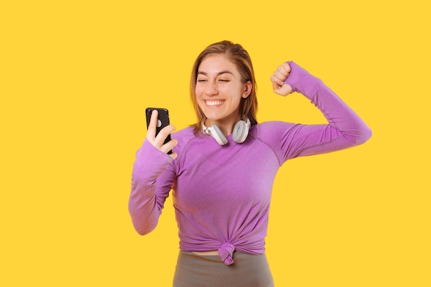 Kobieta w stroju sportowym, trzymając telefon, wykonuje gest zwycięzcy