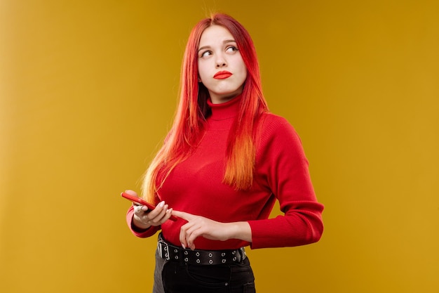 Kobieta w stylu glamour z rudymi włosami używająca smartfona na żółtym tle