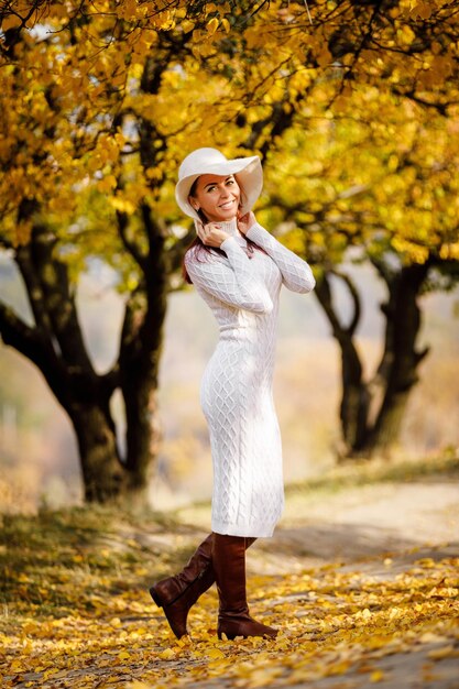 Kobieta w sukience i kapeluszu na tle jesiennych liści