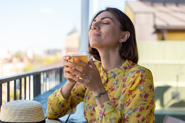 Kobieta w sukience w letniej kawiarni ciesząc się chłodną kombucha szklanką piwa