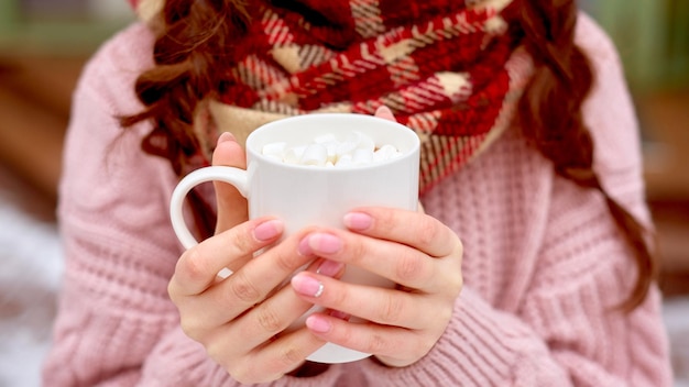 Kobieta w szaliku w kratkę pije gorącą kawę z pianką zbliżenie ręce z filiżanką kakao
