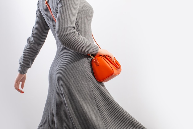 Kobieta w szarej dżersejowej sukience z pomarańczową torebką na białym tle