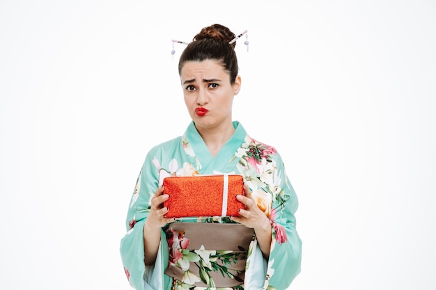 Zdjęcie kobieta w tradycyjnym japońskim kimonie trzymająca prezent ze smutnym wyrazem twarzy na białym tle