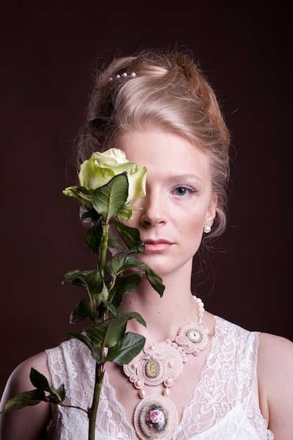 Kobieta w wiktoriańskiej sukni zakrywającej oko różą. Bogaty i vintage. Luksus i elegancja. Zdjęcie studyjne