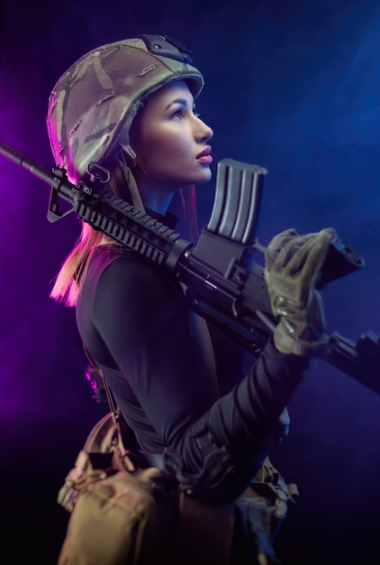 Kobieta w wojskowym mundurze airsoftowym z amerykańskim karabinem automatycznym i hełmem na ciemnym tle