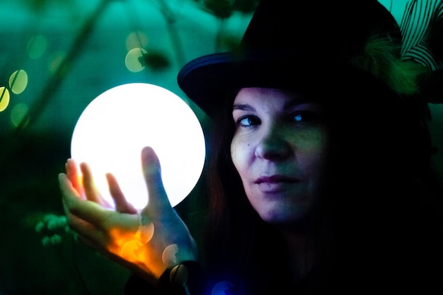 Kobieta w wysokim kapeluszu ze świecącą kulą w dłoniach. kula świeci, światła latają dookoła