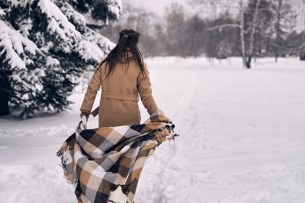 Kobieta w zaśnieżonym lesie owinięta kocem Kobieta ciesząca się zimowymi chwilami w zaśnieżonym parku