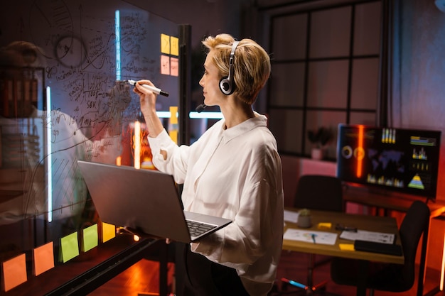 Kobieta w zestawie słuchawkowym za pomocą laptopa do sprawdzania postępu pracy z tablicą kanban