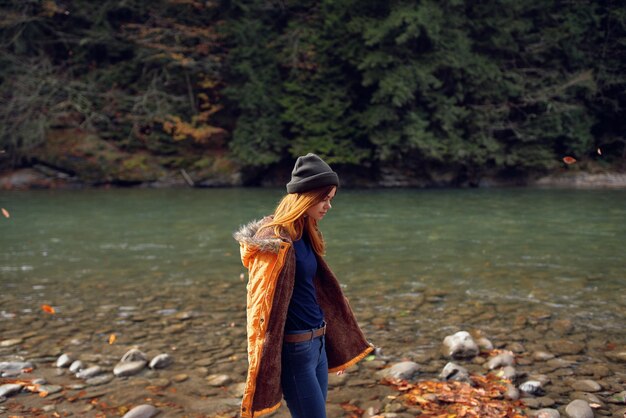 Kobieta w żółtej kurtce nad rzeką podziwia przyrodę jesienny las