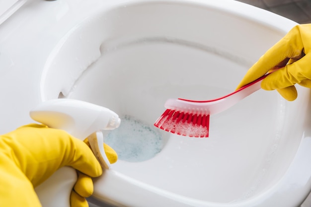 Kobieta w żółtych gumowych rękawiczkach czyści muszlę klozetową czerwoną szczotką i detergentem