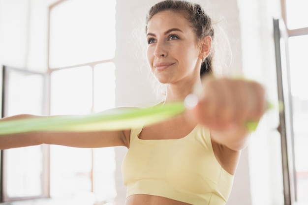 Kobieta w żółtym sportowym topie robi trening z zielonym hula hop.