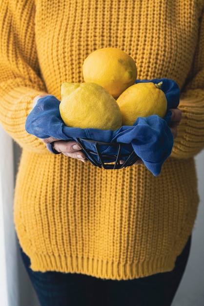 Kobieta w żółtym swetrze trzymająca świeże cytryny