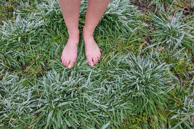Zdjęcie kobieta wcześnie rano chodzi boso po zamarzniętej trawie pokrytej szronem utwardzającym jej ciało odmładzanie ciała energia ziemi
