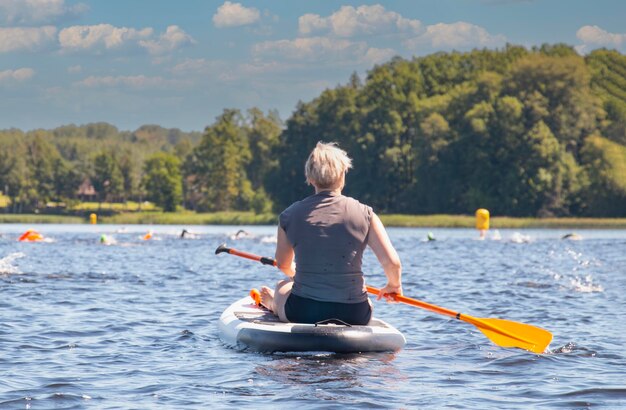 Kobieta wiosłuje na deskach SUP na dużej rzece podczas wyścigu pływaków Stand up paddle boarding jest świetną aktywnością na świeżym powietrzu w letni dzień