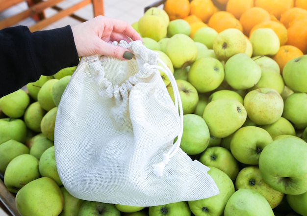 Kobieta wkłada jabłka do torby na zakupy wielokrotnego użytku. Zero marnowania. Ekologiczne i przyjazne środowisku opakowania. Tkaniny płócienne i lniane. Zapisz koncepcję natury. Brak plastiku jednorazowego użytku w supermarketach.