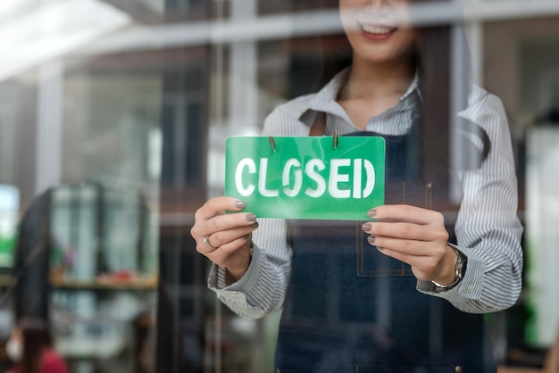 Kobieta właściciel małej firmy trzyma zamknięty znak w kawiarni.