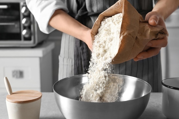 Kobieta wlewa mąkę do miski na stole