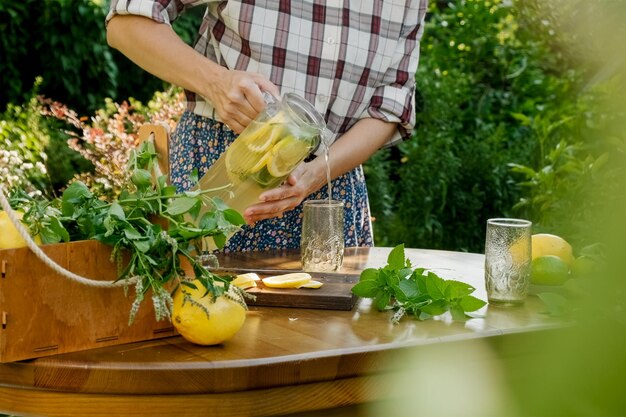 Kobieta wlewająca domową lemoniadę do szklanki w letnim ogrodzie