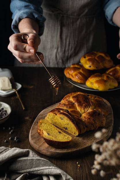 Kobieta wręcza dolewanie miód na świeżym piec brioche na ciemnym drewnianym tle