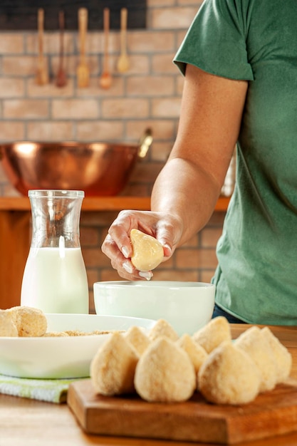 Kobieta wręcza panierowanie brazylijskiego krokieta coxinha de frango z bułką tartą na drewnianym stole w kuchni